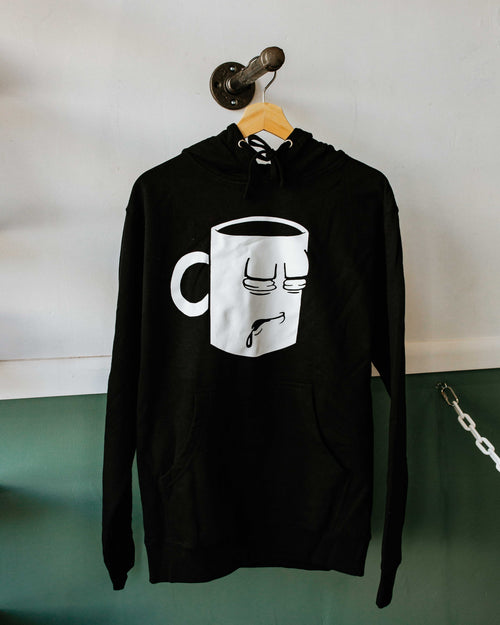 A Tired Eyes Coffee Classic Mug Hoodie with a white print on black hoodie.