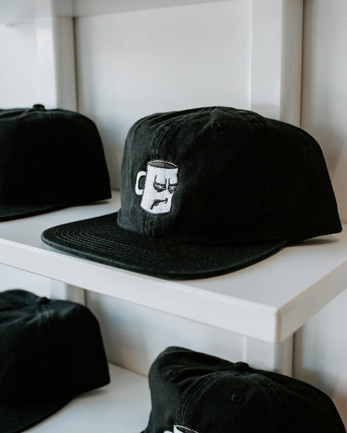 A black and white hat from with an embroidered logo from Tired Eyes Coffee.