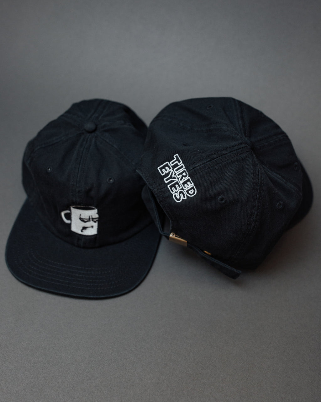 A black and white hat from with an embroidered logo from Tired Eyes Coffee.
