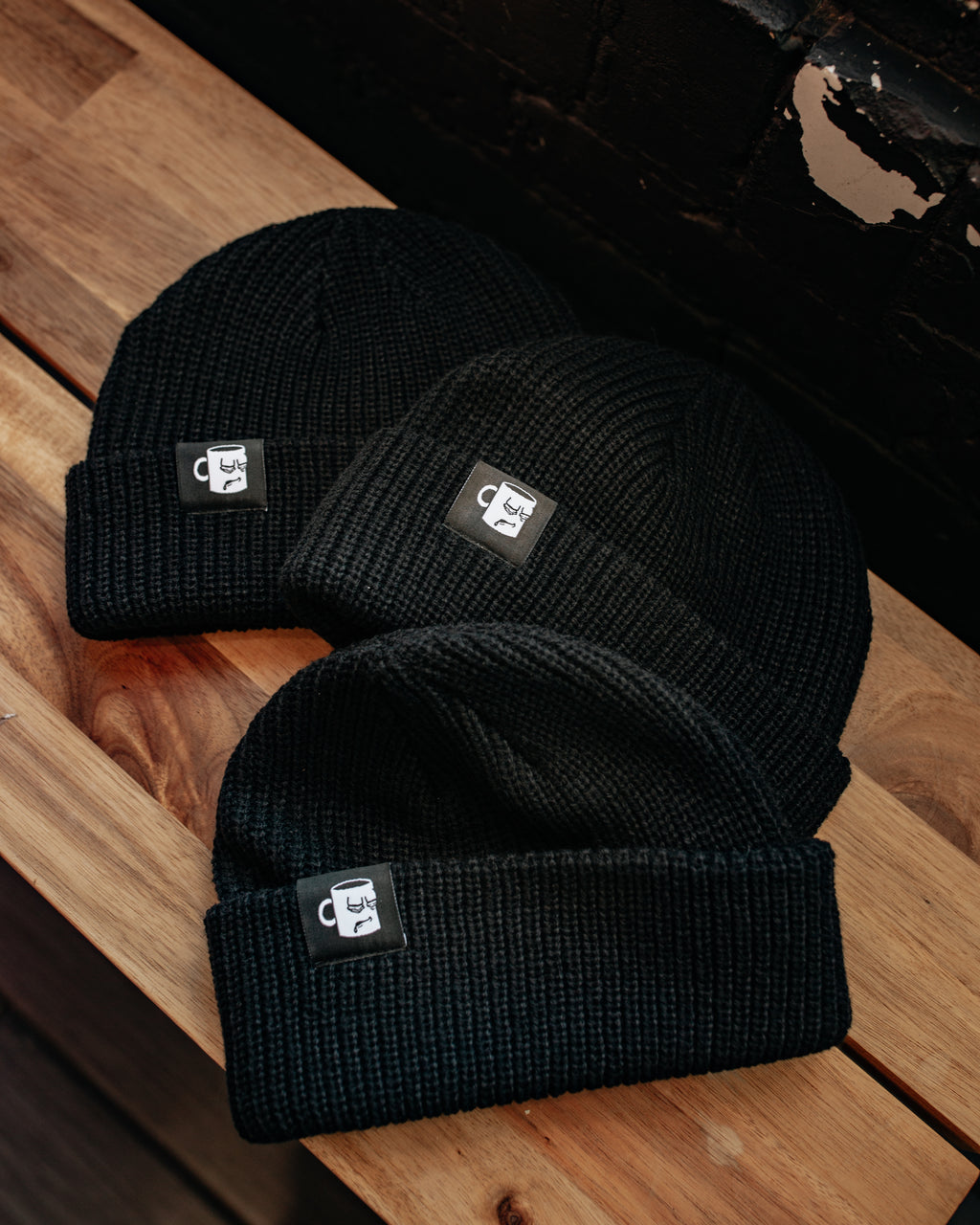 A black and white knit beanie from with an embroidered logo from Tired Eyes Coffee.