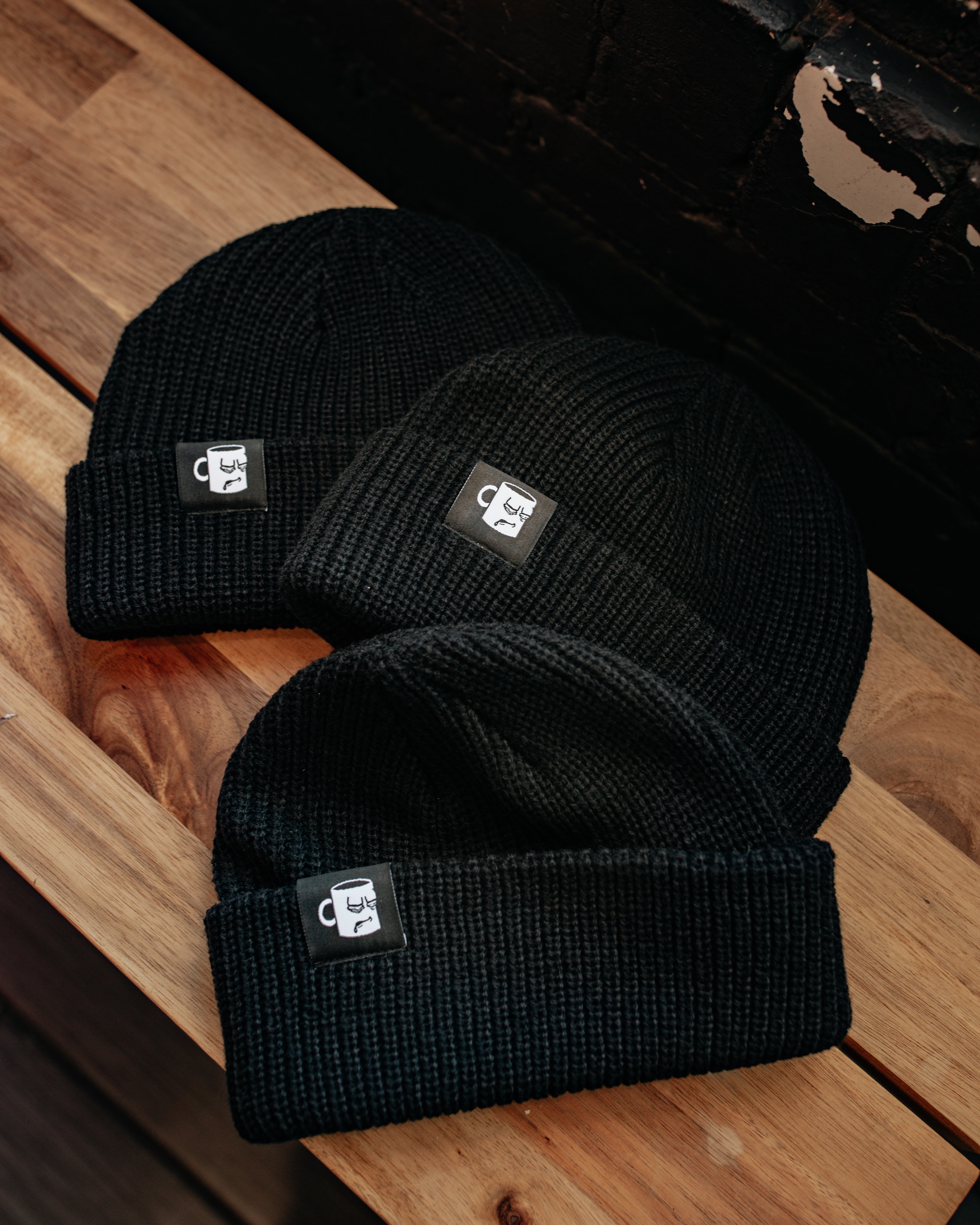 A black and white knit beanie from with an embroidered logo from Tired Eyes Coffee.
